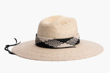 Load image into Gallery viewer, A light beige woven straw wide-brim hat with a black and white braided band around the crown and a black chin cord, shown against a plain white background. Left Side
