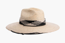Load image into Gallery viewer, A light beige woven straw wide-brim hat with a black and white braided band around the crown and a black chin cord, shown against a plain white background. Right side
